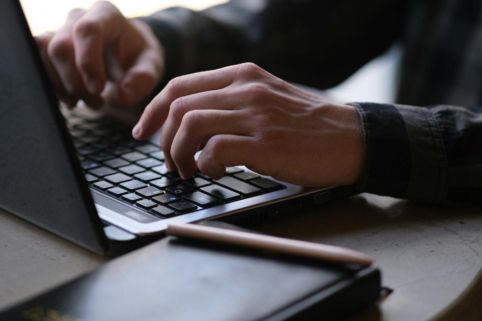 Close-up photo of hands typing on a laptop, working on his digital products