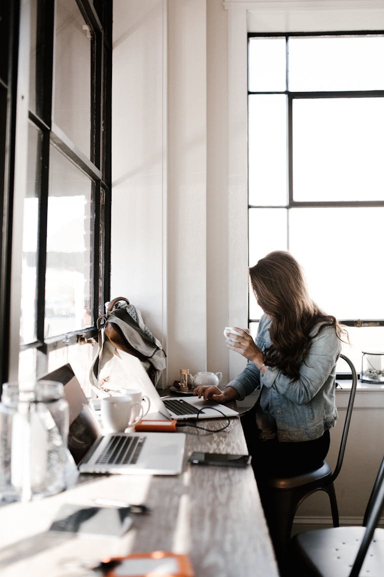 A young woman working on her laptop, sipping coffee in a bright café setting, brainstorming blog post ideas.