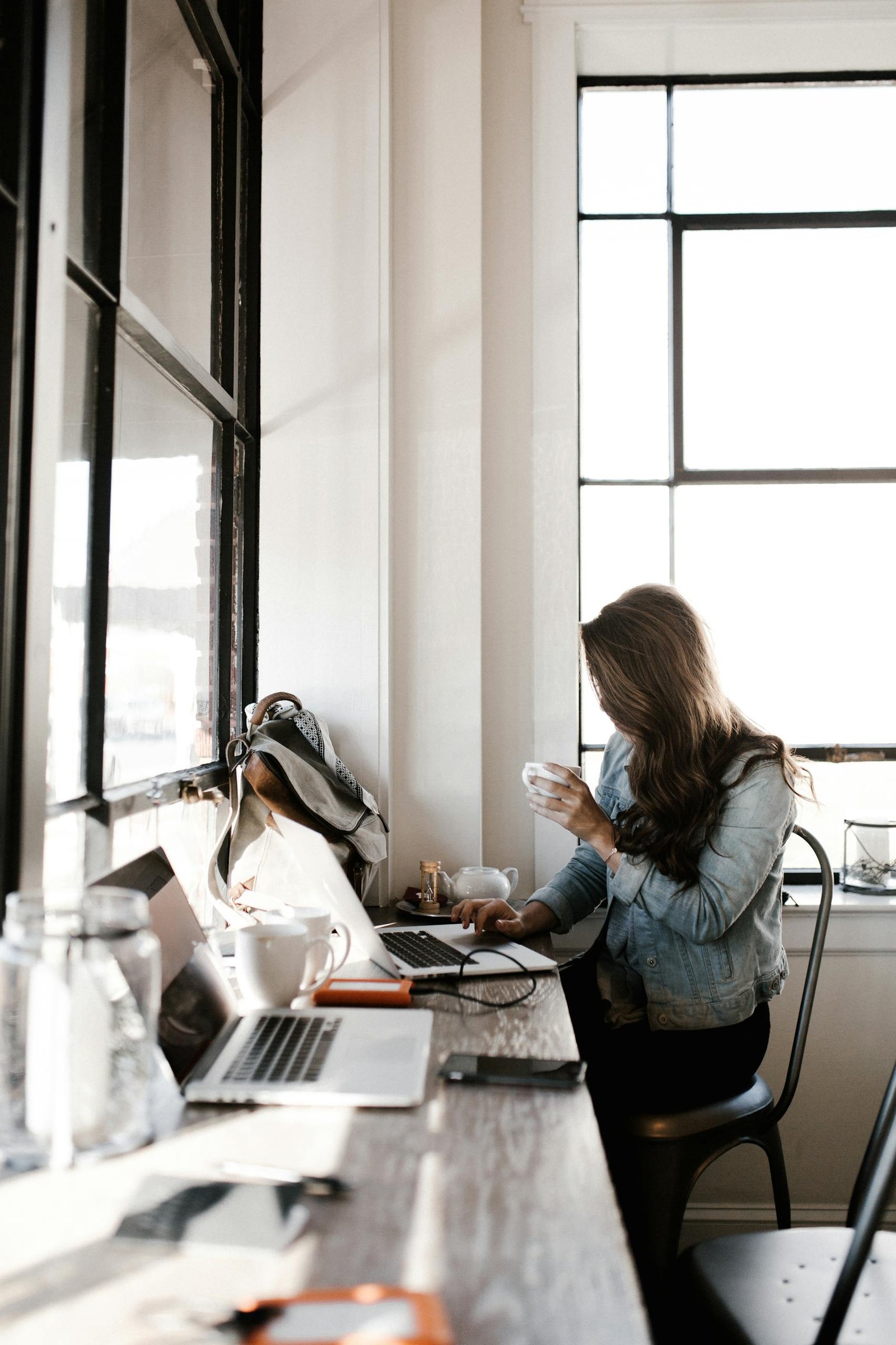 A young woman working on her laptop, sipping coffee in a bright café setting, brainstorming blog post ideas.