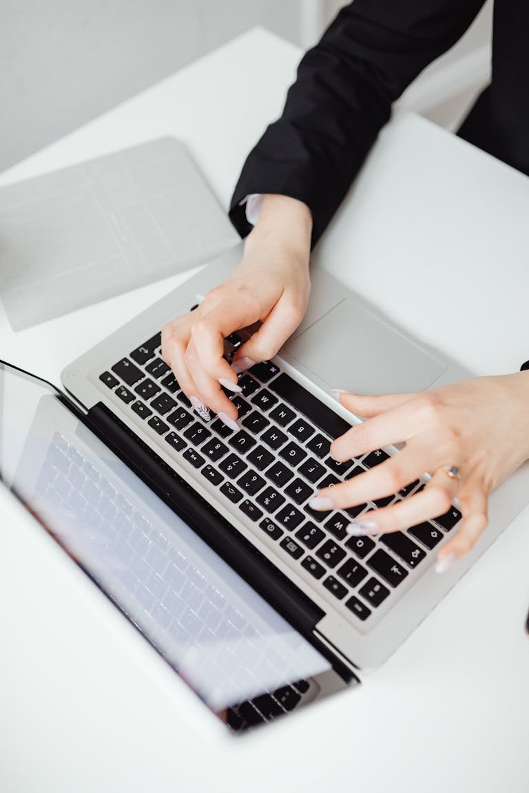 Hands typing on a laptop keyboard on a white desk in an office setting working on blog