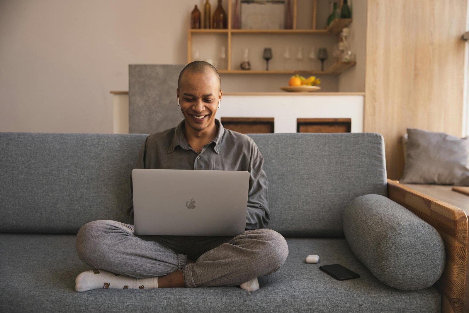 Smiling man using laptop on sofa for remote work, enjoying a cozy home office.