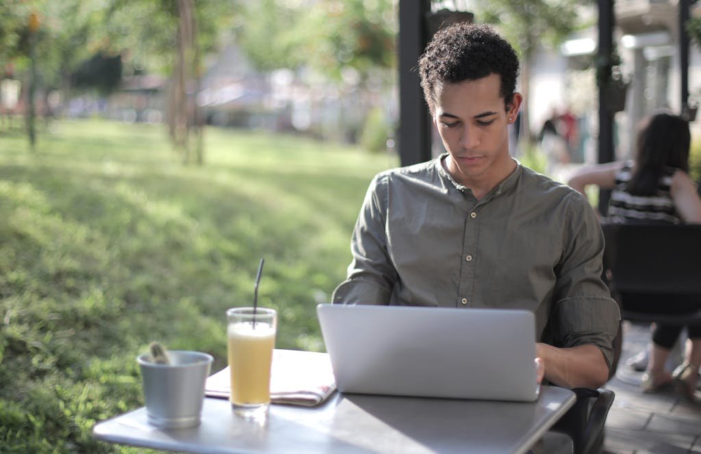 Young man working on a laptop outside in a casual and relaxed setting, enjoying a drink thinking about the purpose of blogging.
