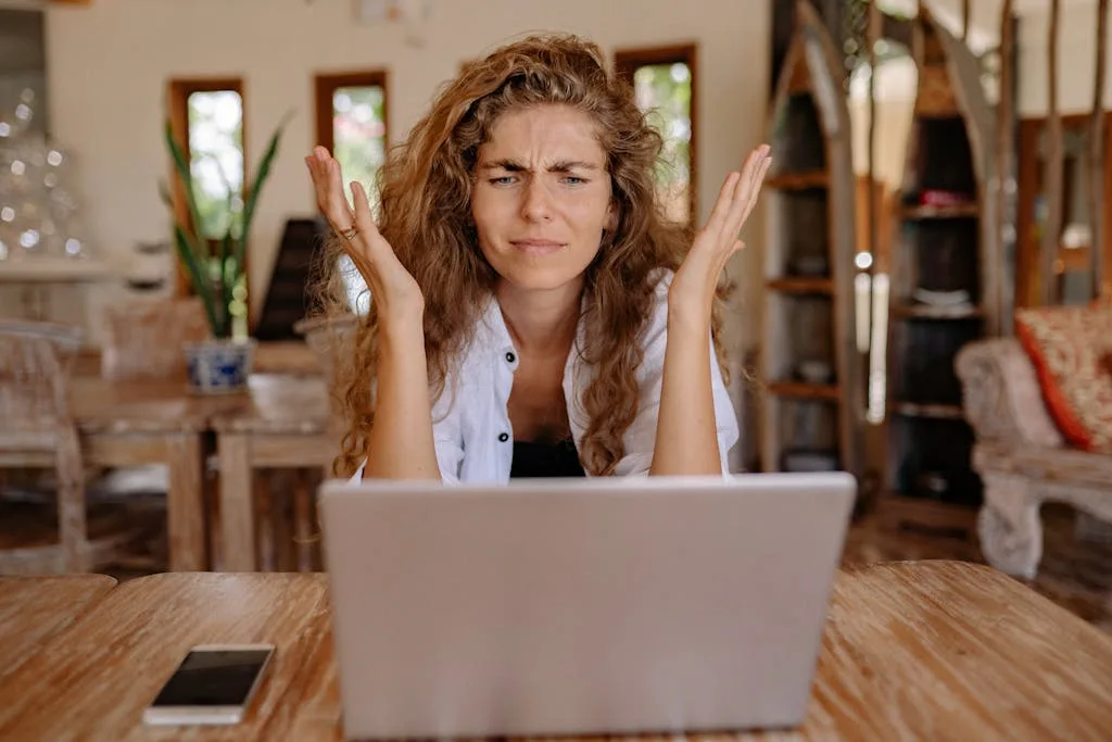 A woman frustrated with her laptop while working remotely indoors, expressing stress making common blogging mistakes
