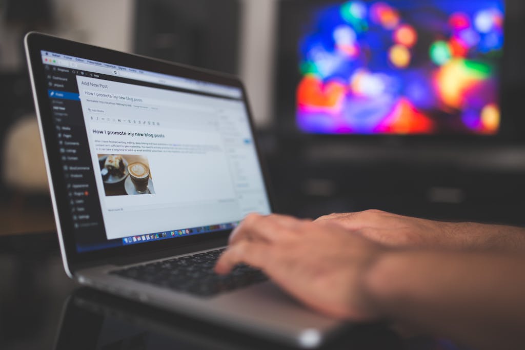 Hands typing on a laptop with a blog post visible, cozy indoor setting with colorful screen in background working on passive income blog